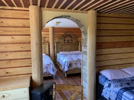 Una habitación de cabaña de madera con dos camas, un escritorio pequeño y un arco de piedra.