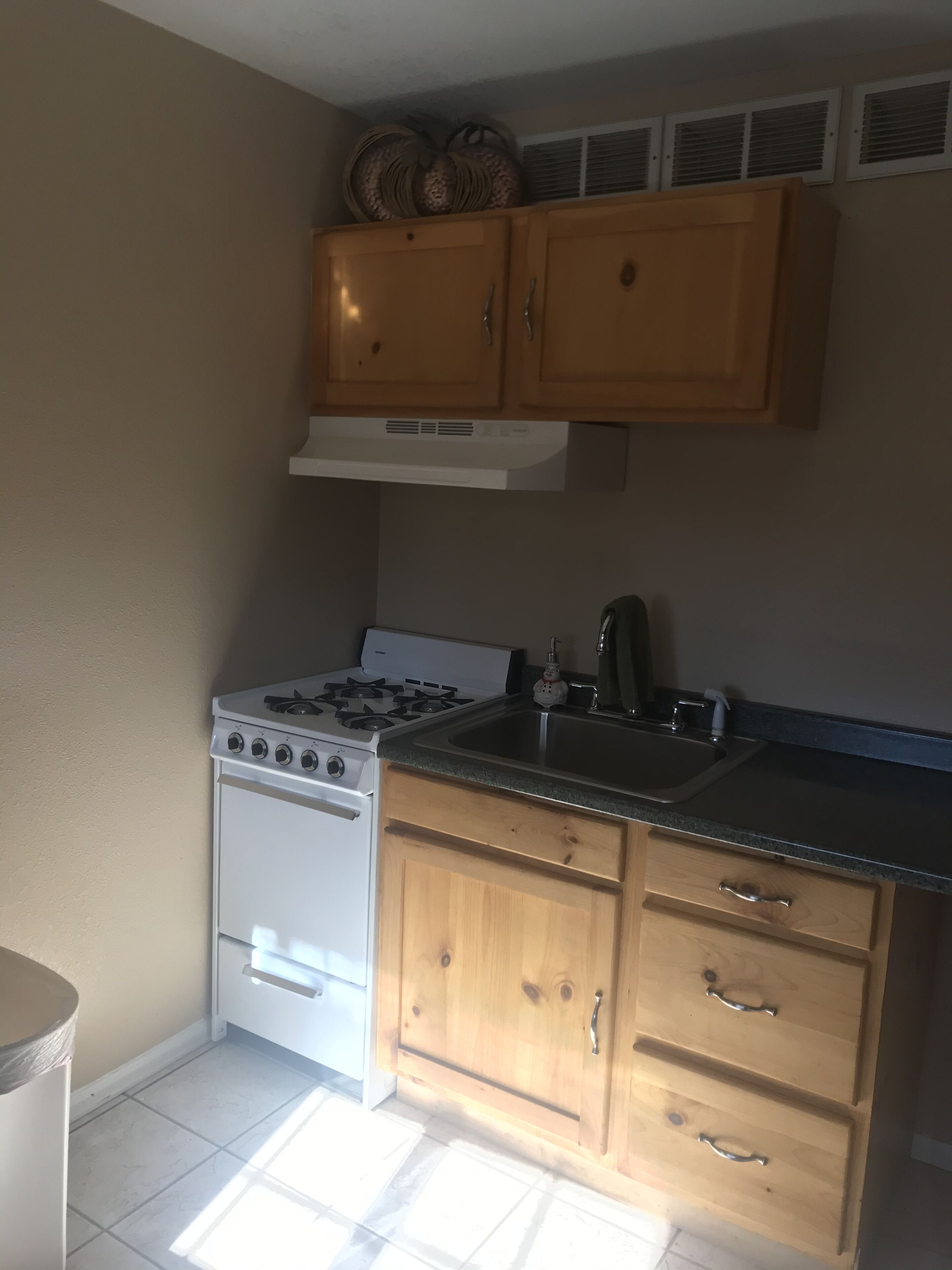 Una cocina con armarios de madera, una estufa blanca, un fregadero y una ventana sobre los armarios.