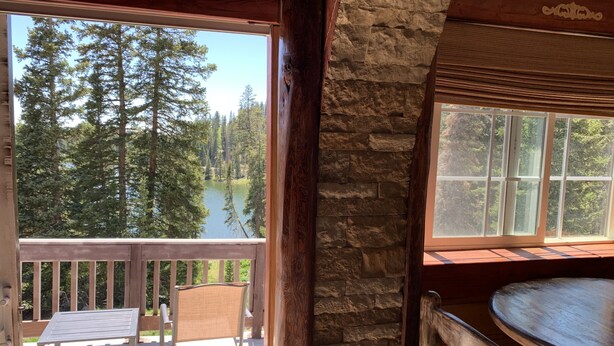 A wooden deck with a table and chairs, a stone wall, and a view of a lake surrounded by trees. - Alexander lake lodge (Cedaredge)