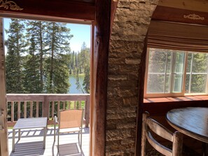 A wooden deck with a table and chairs, a stone wall, and a view of a lake surrounded by trees. - Alexander lake lodge (Cedaredge)