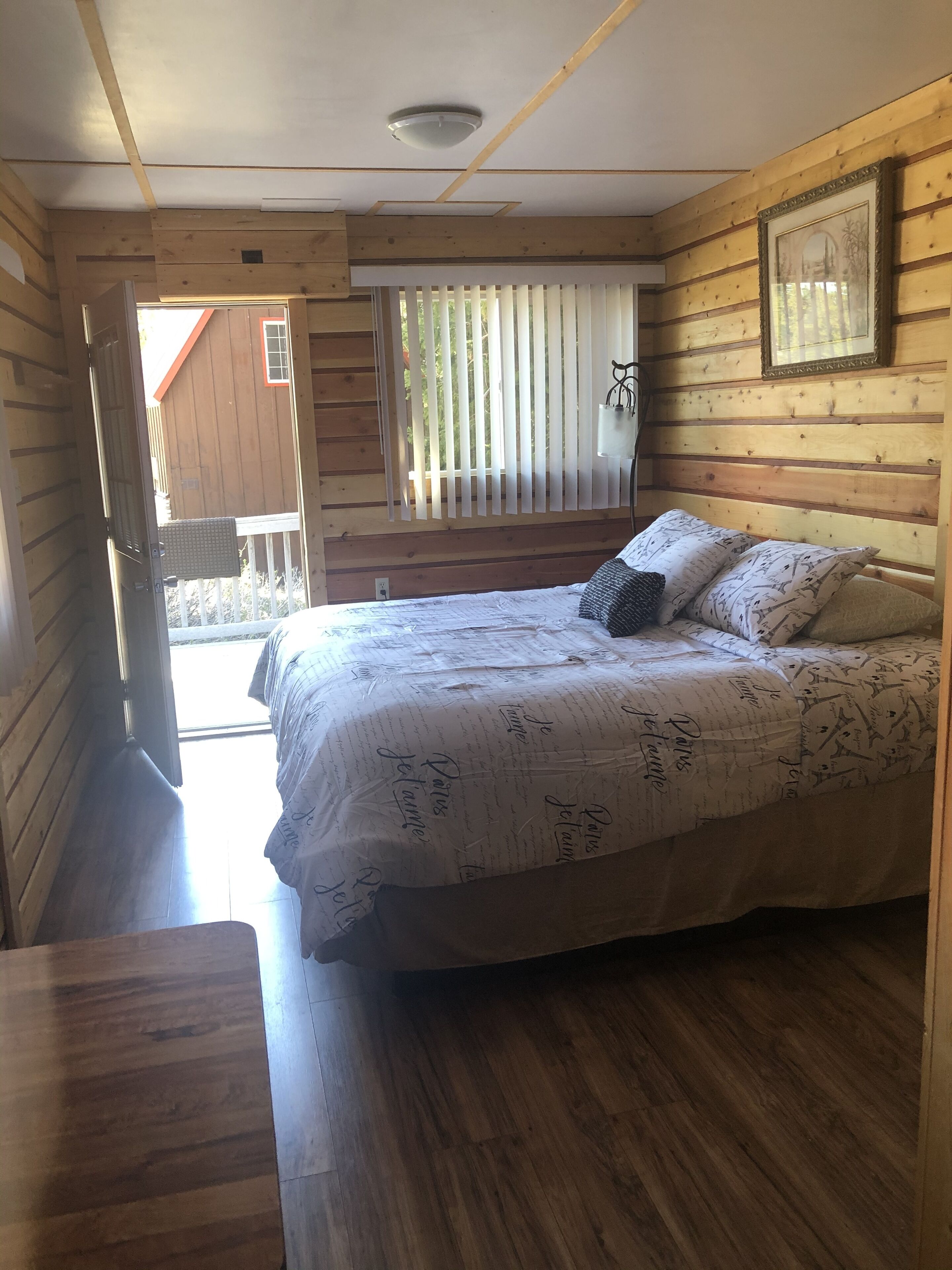 A wooden cabin bedroom with a bed, a window with blinds, and a ceiling light.