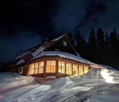 Una cabaña de troncos con amplias ventanas, rodeada de nieve.