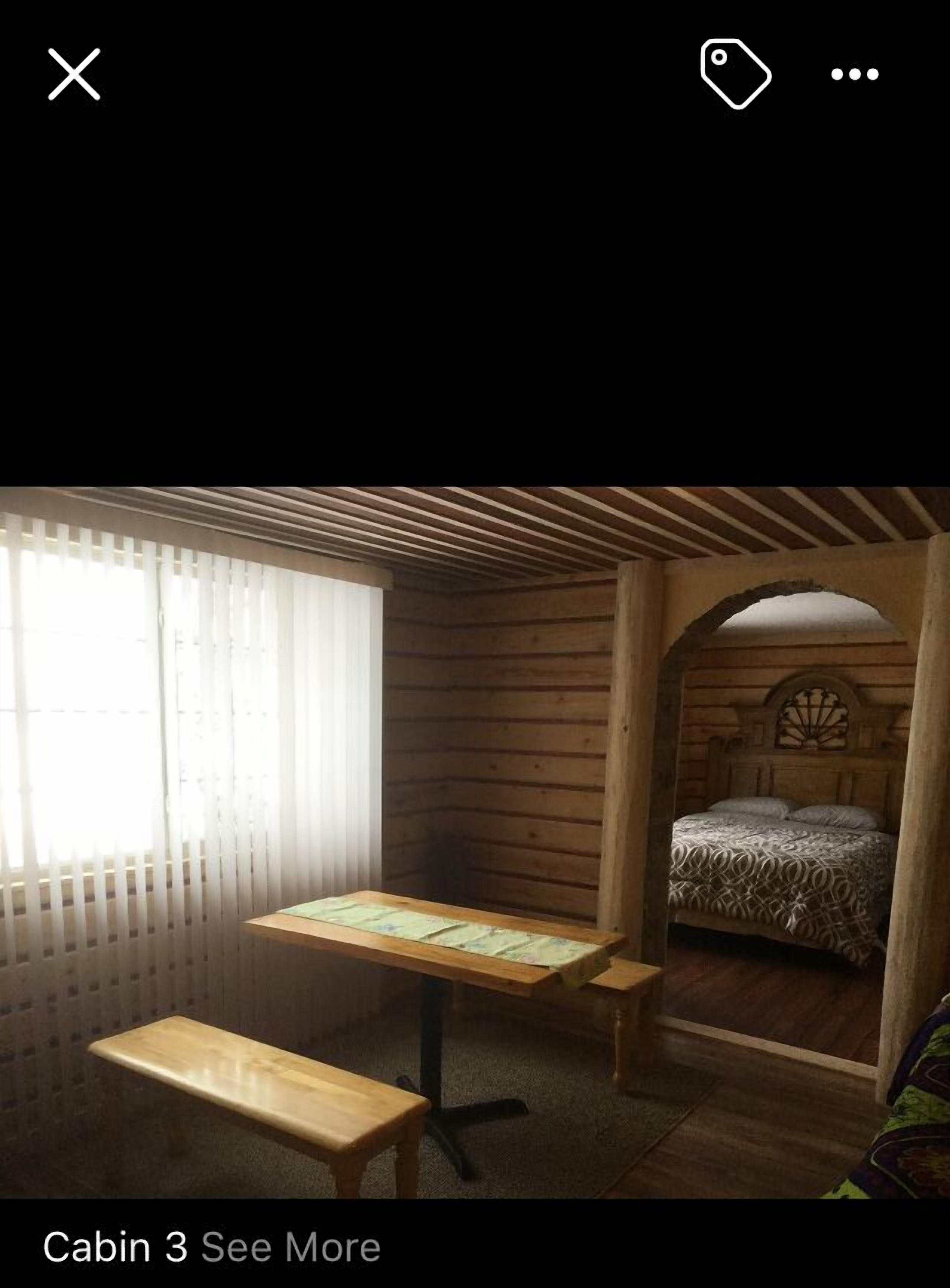 A cabin with a wooden interior, a bed with patterned bedding, a wooden table, and a bench.