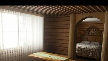 A cabin with a wooden interior, a bed with patterned bedding, a wooden table, and a bench.