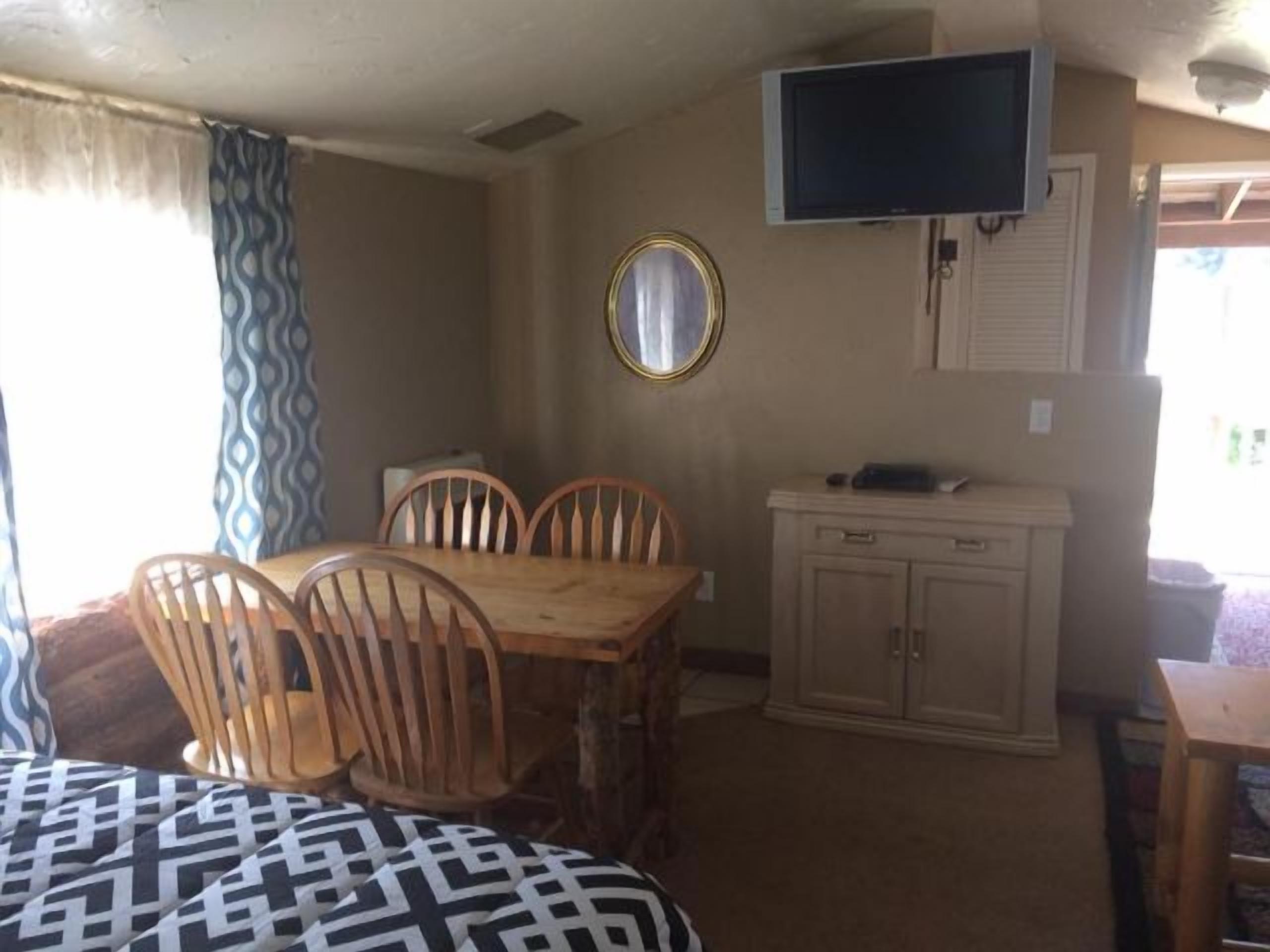 A compact room with a dining table and chairs, a television mounted on the wall, and a small cabinet.