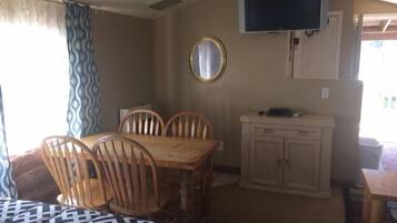 A compact room with a dining table and chairs, a television mounted on the wall, and a small cabinet.