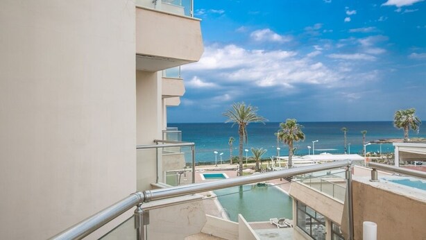 Un balcon avec une piscine et des palmiers, donnant sur l’océan.