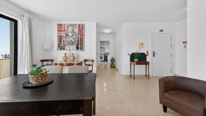 A hotel room with a dining area, a sofa, a painting, and a view of the city.