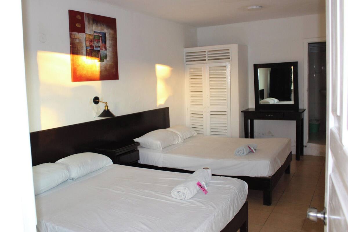 Ein Hotelzimmer mit zwei Betten, einem Schreibtisch, einem Spiegel und einem Gemälde an der Wand.