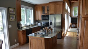 A spacious kitchen with wooden cabinets, a large island, stainless steel appliances, and a view of the outdoors.