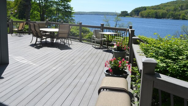 A wooden deck with outdoor furniture, a railing, and a view of a lake.
