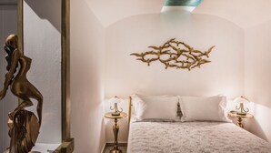 Un dormitorio con cama, dos mesitas de noche con lámparas, una lámpara de pared y una escultura decorativa.