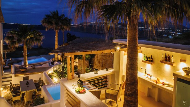 Un área de bar al aire libre con piscina, sillones de descanso y vistas de la ciudad de noche.
