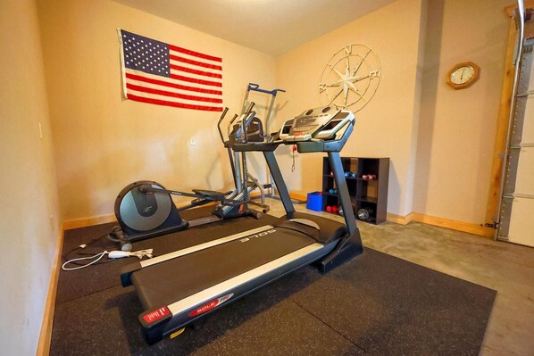 A home gym with a treadmill, elliptical, and weights.