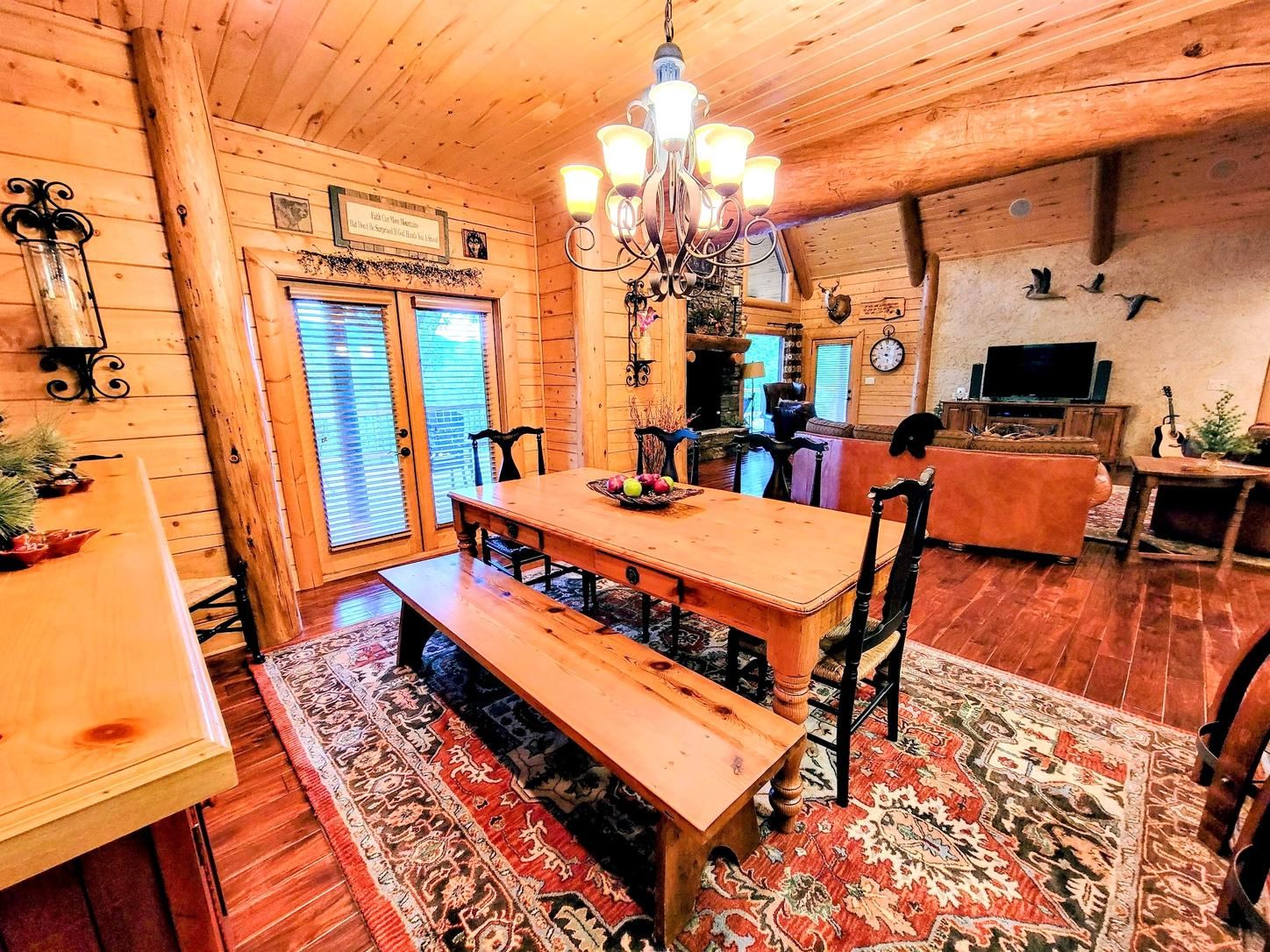 A wooden interior with a dining table, benches, a chandelier, and a television.