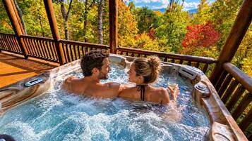 A hot tub with a wooden deck and a view of trees and mountains.