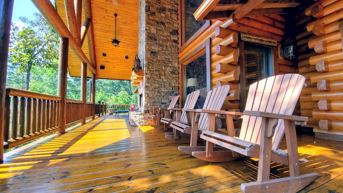 A wooden deck with Adirondack chairs, a stone wall, and a wooden ceiling.