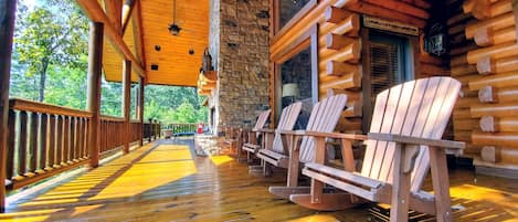 A wooden deck with Adirondack chairs, a stone wall, and a wooden ceiling.