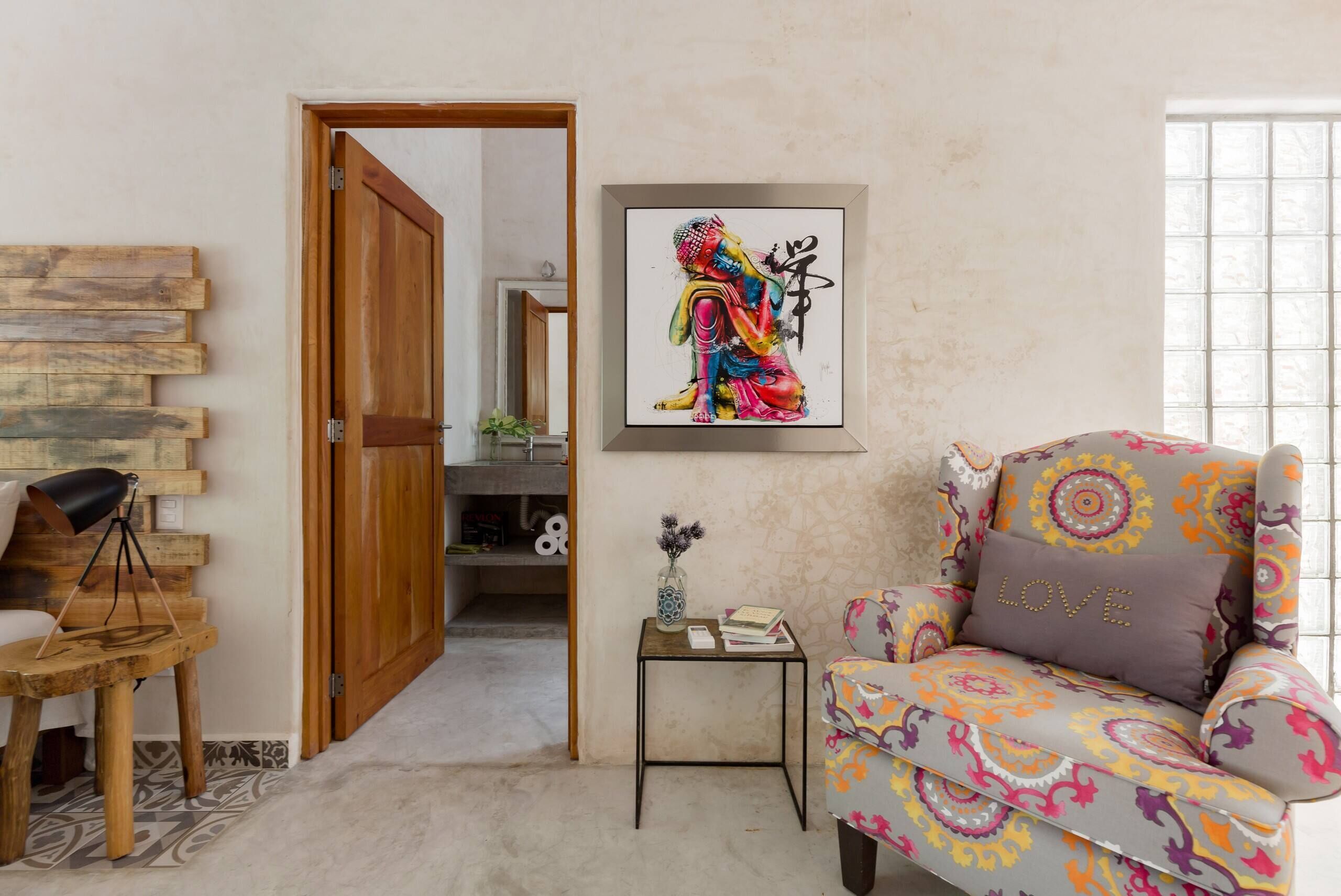 Ein Zimmer mit Holztür, einem farbenfrohen gemusterten Sessel, einem kleinen Beistelltisch mit einer Vase und einem gerahmten Kunstwerk an der Wand.