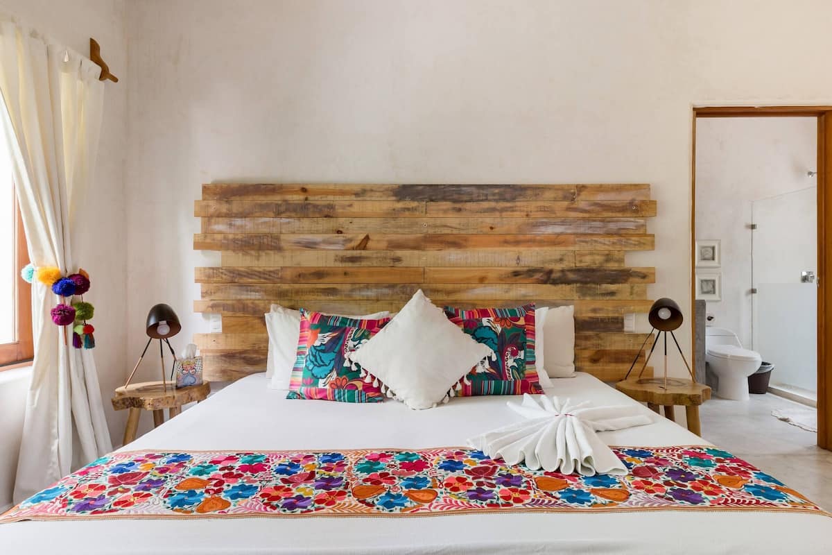 Ein Hotelzimmer mit Holzkopfteil, farbenfroher floraler Bettdecke, weißen Kissen und einem ordentlich bezogenen Bett mit einem weißen Handtuch.