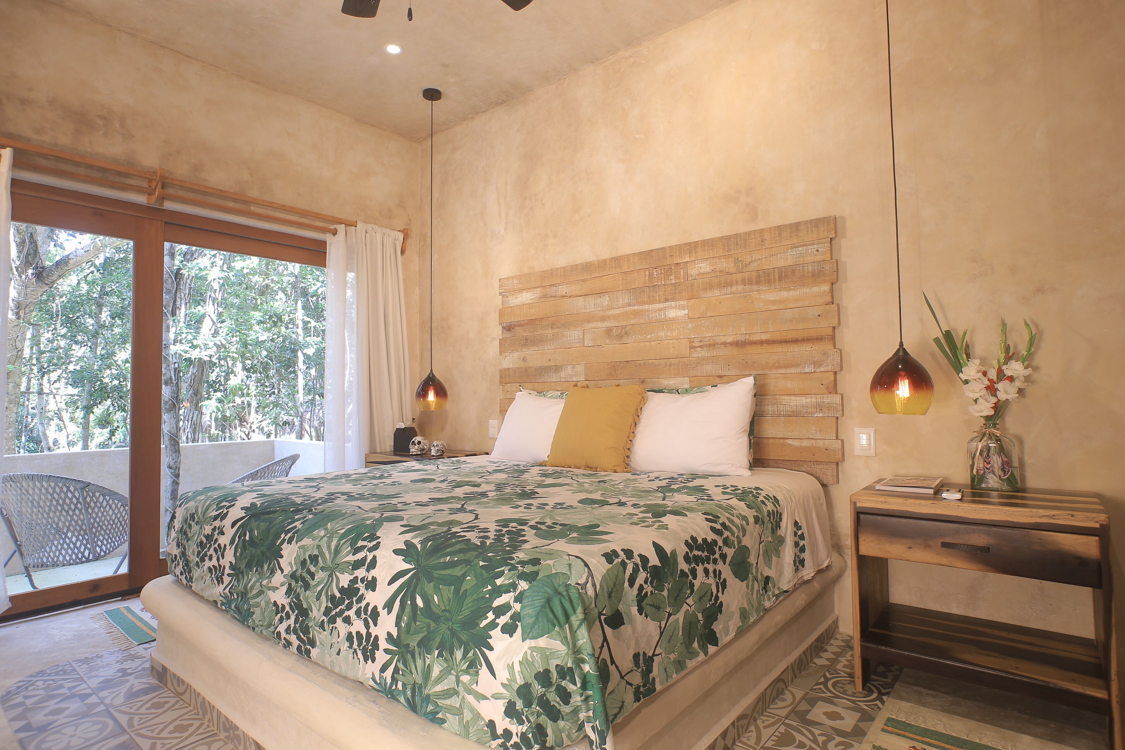 Un dormitorio con una cama grande, cabecera de madera, mesita de noche y ventana con vistas a árboles.