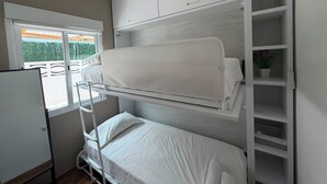 Et værelse med køjeseng, et vindue, et hvidt skab og en hyldeenhed.