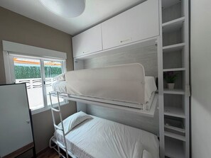 Una stanza con letto a castello, una finestra, un armadio bianco e una scaffalatura.