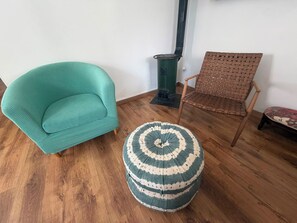 A room with a teal armchair, a woven chair, and a round ottoman.