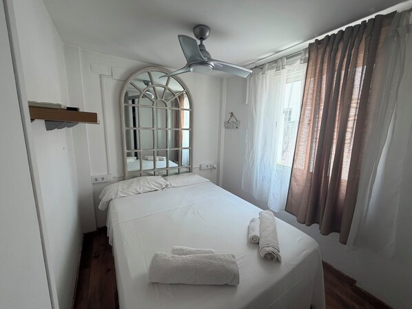 A hotel room with a bed, a ceiling fan, a window with curtains, and a wall-mounted mirror.