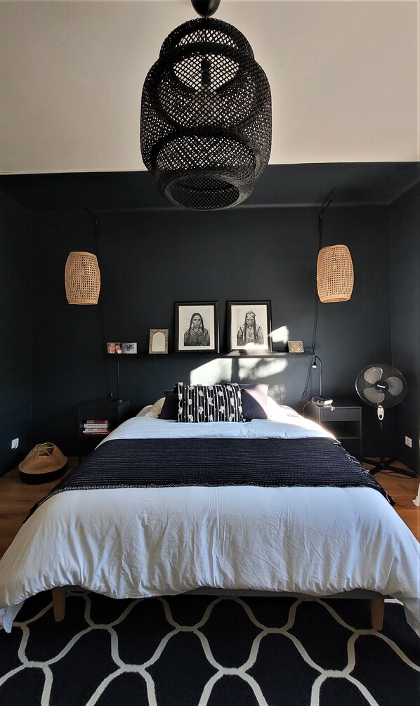A bedroom with a bed, two wall-mounted lamps, a fan, and framed pictures on the wall.