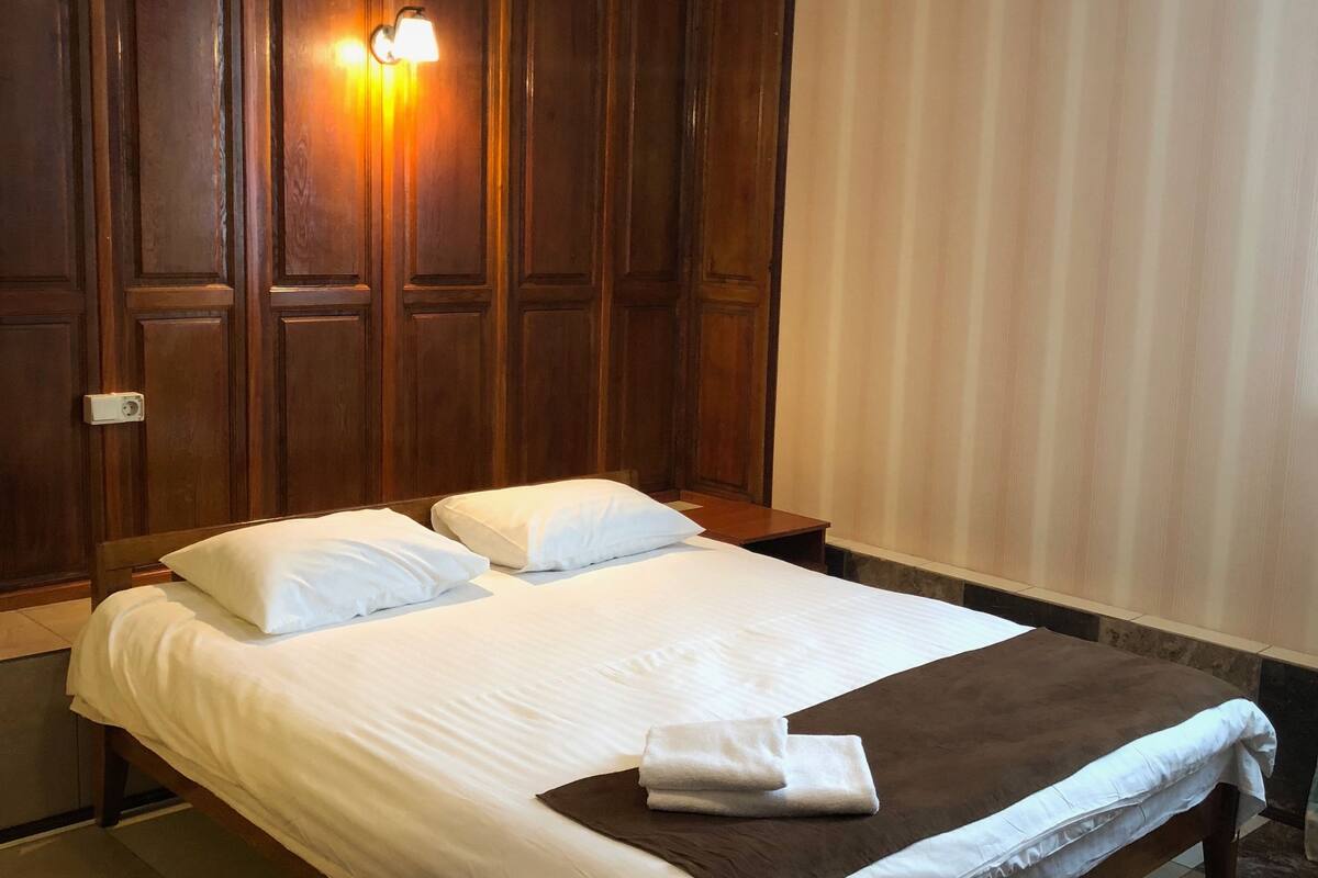A hotel room with a large bed, wooden paneling on the walls, and a light fixture above the bed.