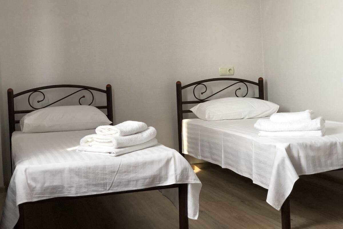 Two single beds with white linens and towels, a wooden headboard, and a light switch on the wall.