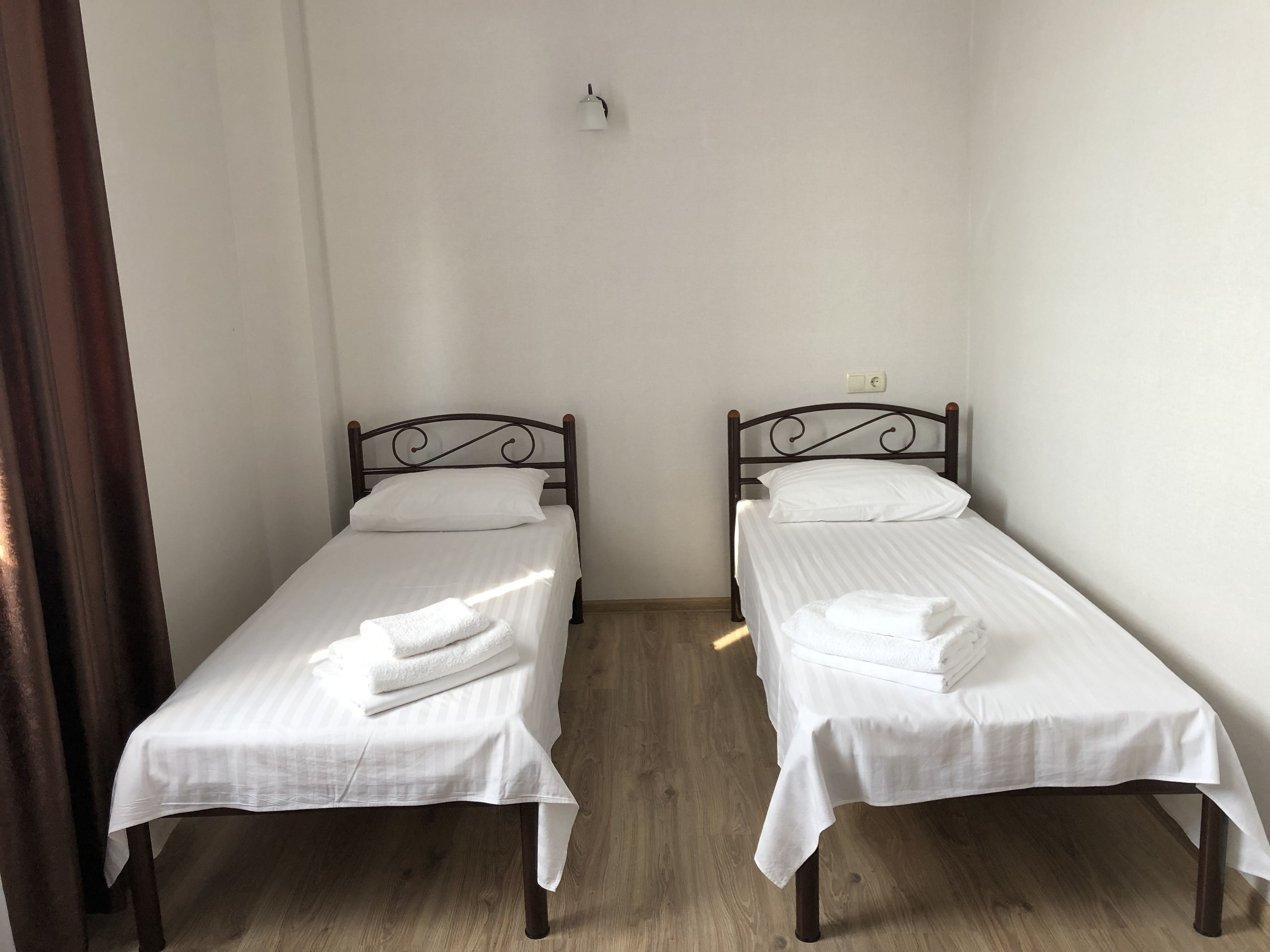 Two single beds with white linens and dark metal frames in a small room with wooden flooring.