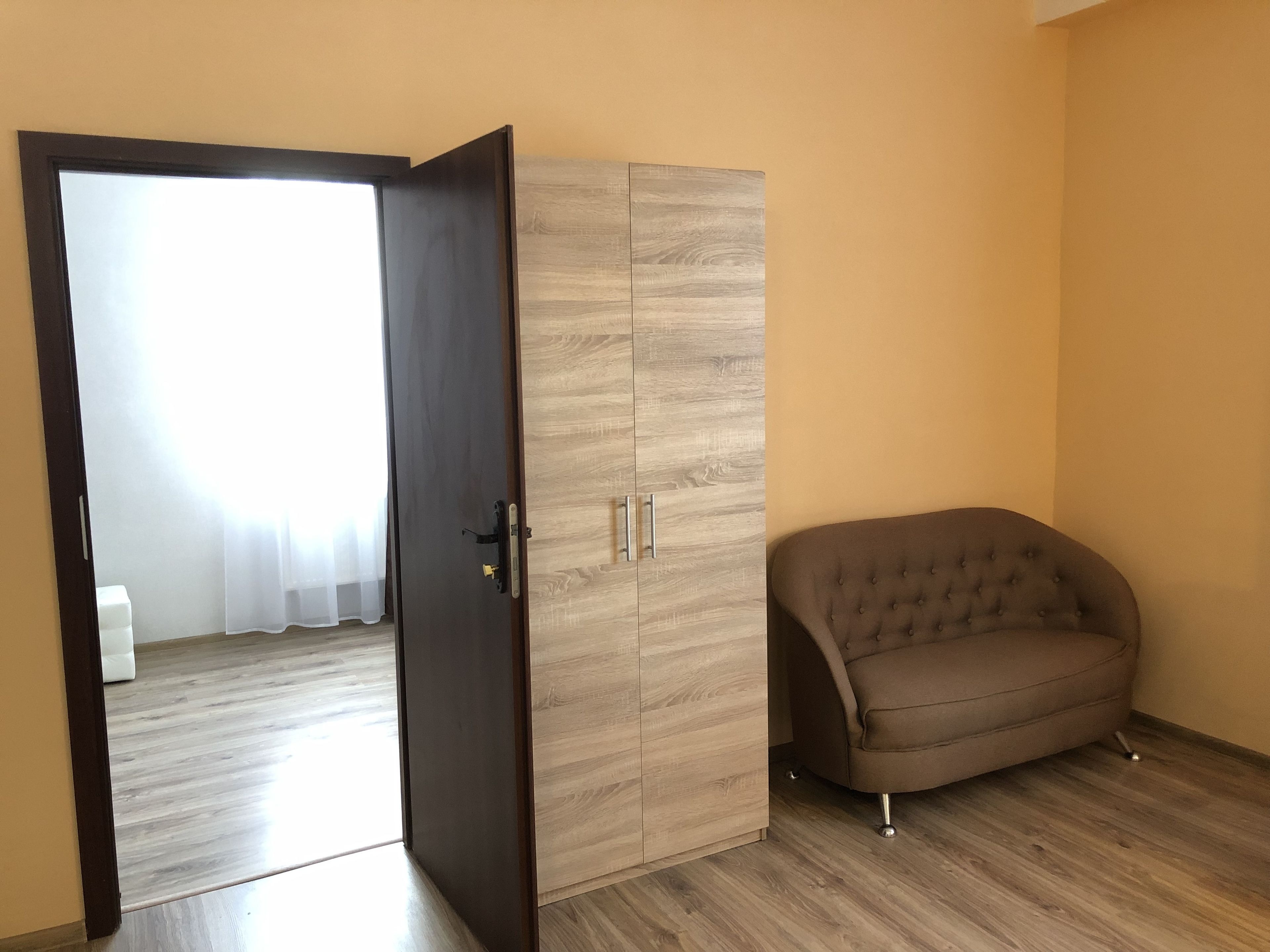 A room with a wardrobe, a brown sofa, and a door leading to another room.