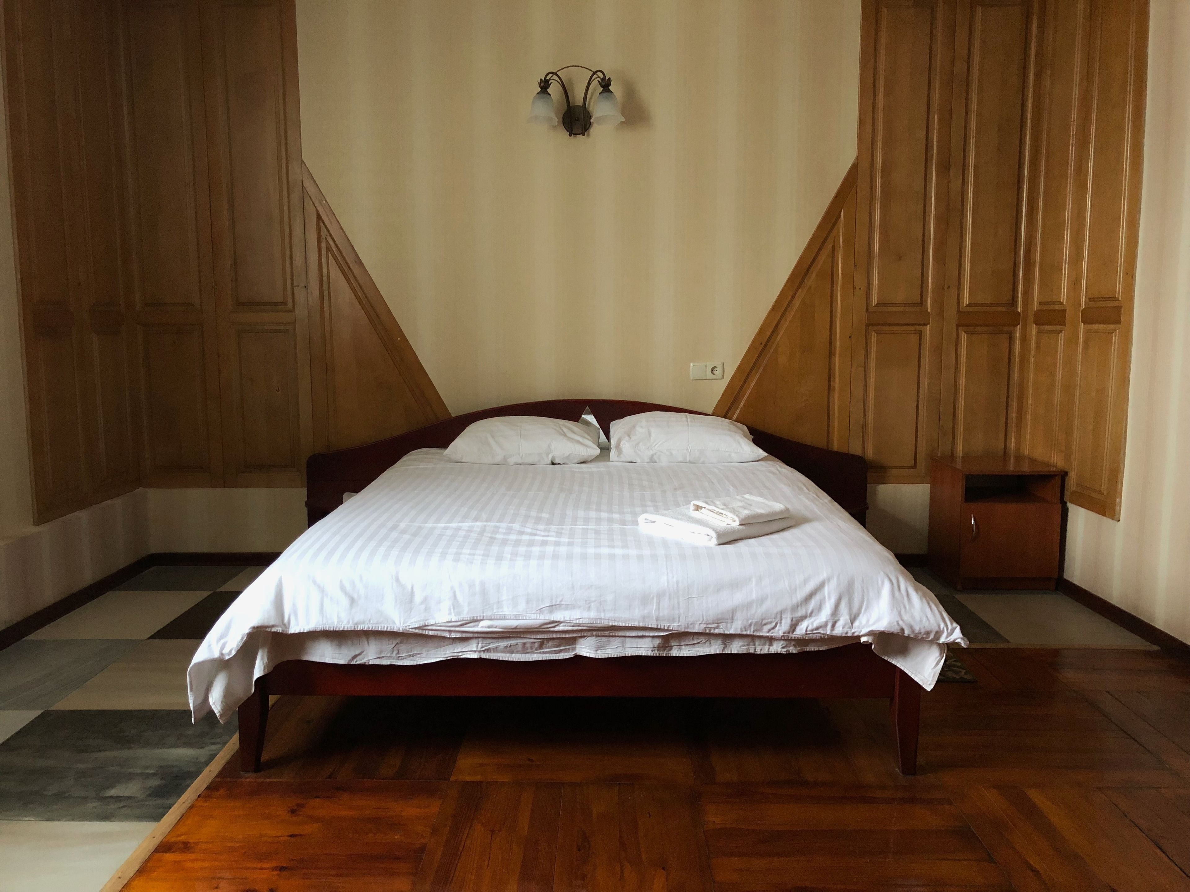 A neatly made bed with white linens and a folded towel, wooden headboard, and a small bedside table.