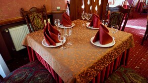 A dining table set with red napkins, wine glasses, and plates, covered by a patterned tablecloth. - Hotel & Restaurant Zhuliany City (Sofiivska Borschahivka)