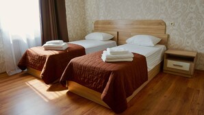 A hotel room with two beds, each with a brown bedspread and white pillows, a wooden nightstand with a drawer, and a patterned wallpaper. - Hotel & Restaurant Zhuliany City (Sofiivska Borschahivka)