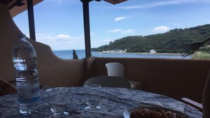 A table with a water bottle, glasses, and pasta dishes, overlooking a coastal view with boats and buildings.