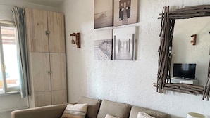 A living room with a L-shaped sofa, a matching ottoman, a television on a wooden stand, and a rustic wall decor.