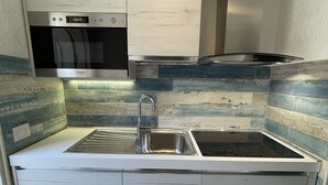 A compact kitchen with a built-in microwave, stainless steel sink, and a range hood.