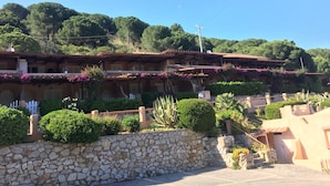 A traditional building with a stone wall and a tiled roof, surrounded by lush greenery and trees.