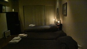 A dimly lit hotel room with two beds, a nightstand, and a radiator. - Apartamentos MDZ - Apart Hotel (Mendoza)