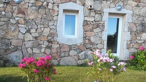 Un bâtiment en pierre doté de deux fenêtres et d’une pelouse bien entretenue, agrémentée de fleurs roses.