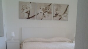 Une chambre à coucher comprenant un lit, une table de chevet et trois tableaux représentant des fleurs, accrochés au mur.