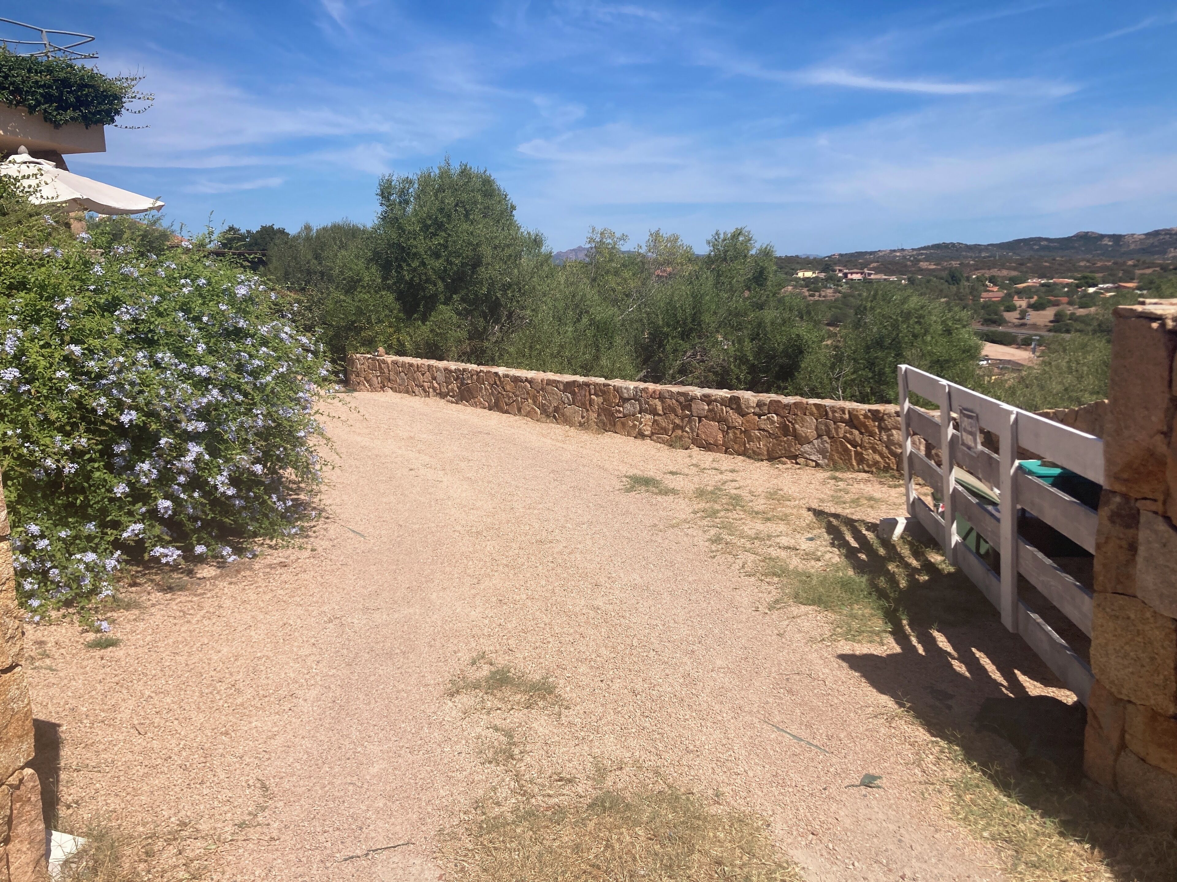 A gravel path leading to a stone wall with a wooden fence on the right.