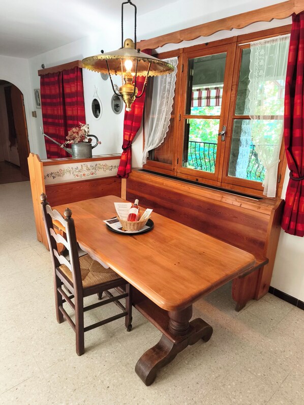 Une table à manger en bois, accompagnée d’un banc, d’un luminaire suspendu et d’une fenêtre avec des rideaux.