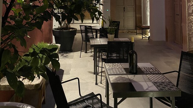Un patio con mesas al aire libre, plantas en macetas y un arco que da a un edificio.