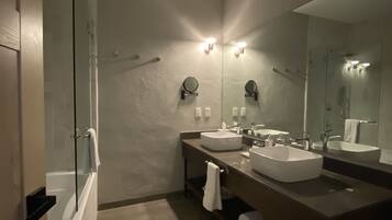 Un baño moderno con un espejo grande, dos lavamanos y una cabina de ducha con paredes de vidrio.
