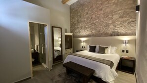 Un dormitorio con pared de piedra, una cama grande, un banco y un espejo.