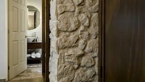 Un pasillo con pared de piedra, puerta de madera y baño con lavamanos y toallas.